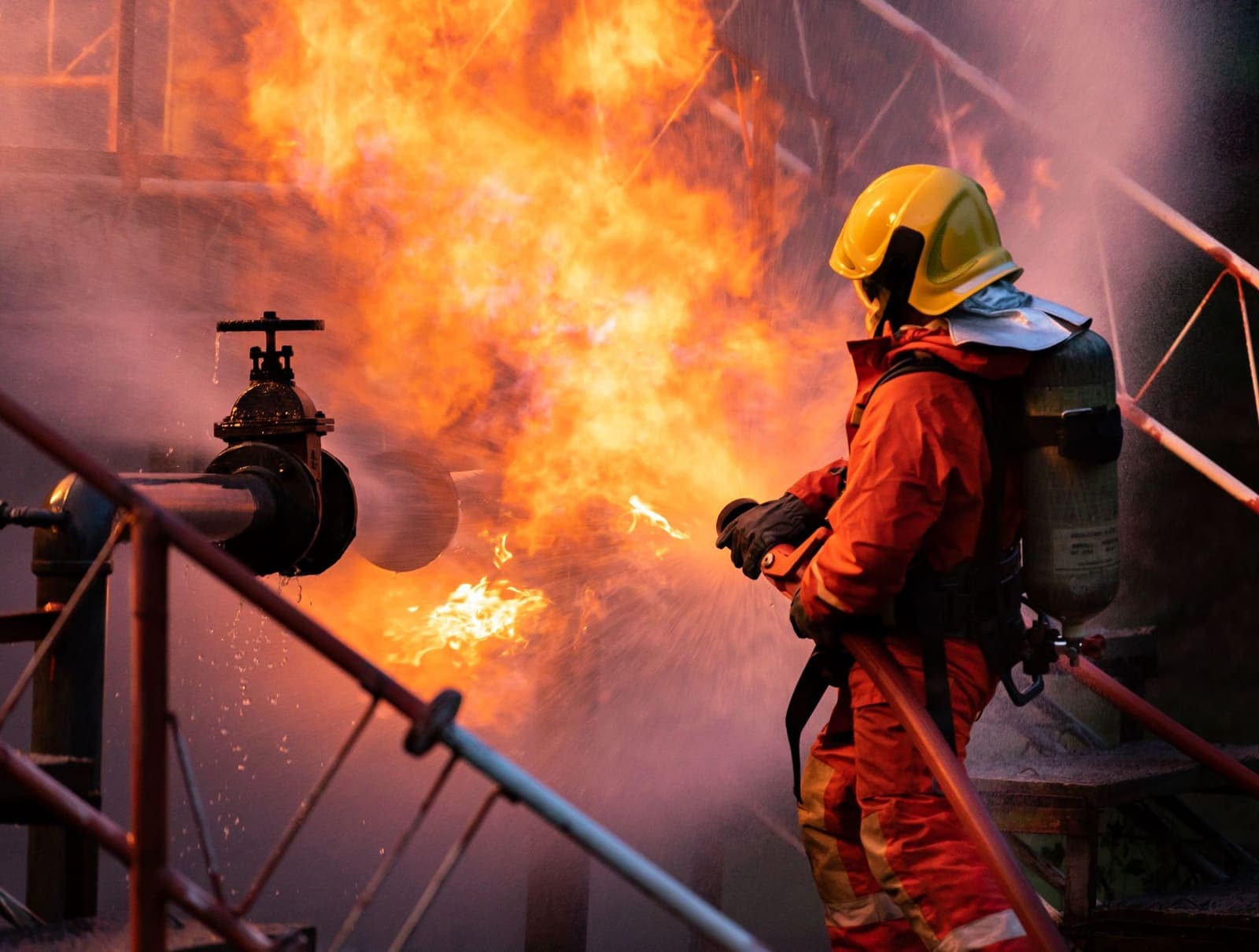 Firefighter using a water-fog extinguisher on a fuel-pipeline fire — industrial fire safety